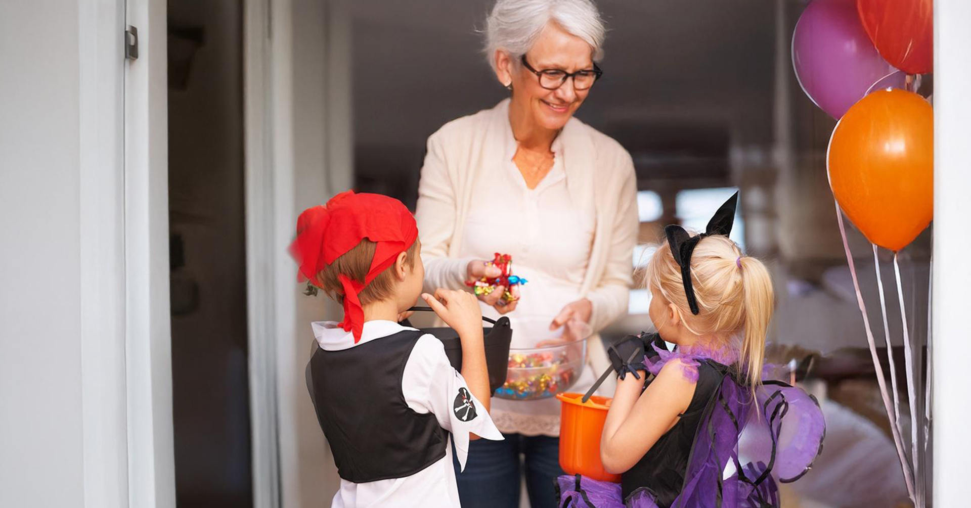 Homemade apple pie senior woman handing out candy to 2 kids trick-or-treating -- one dressed up as a pirate, and the other dressed up as a bat