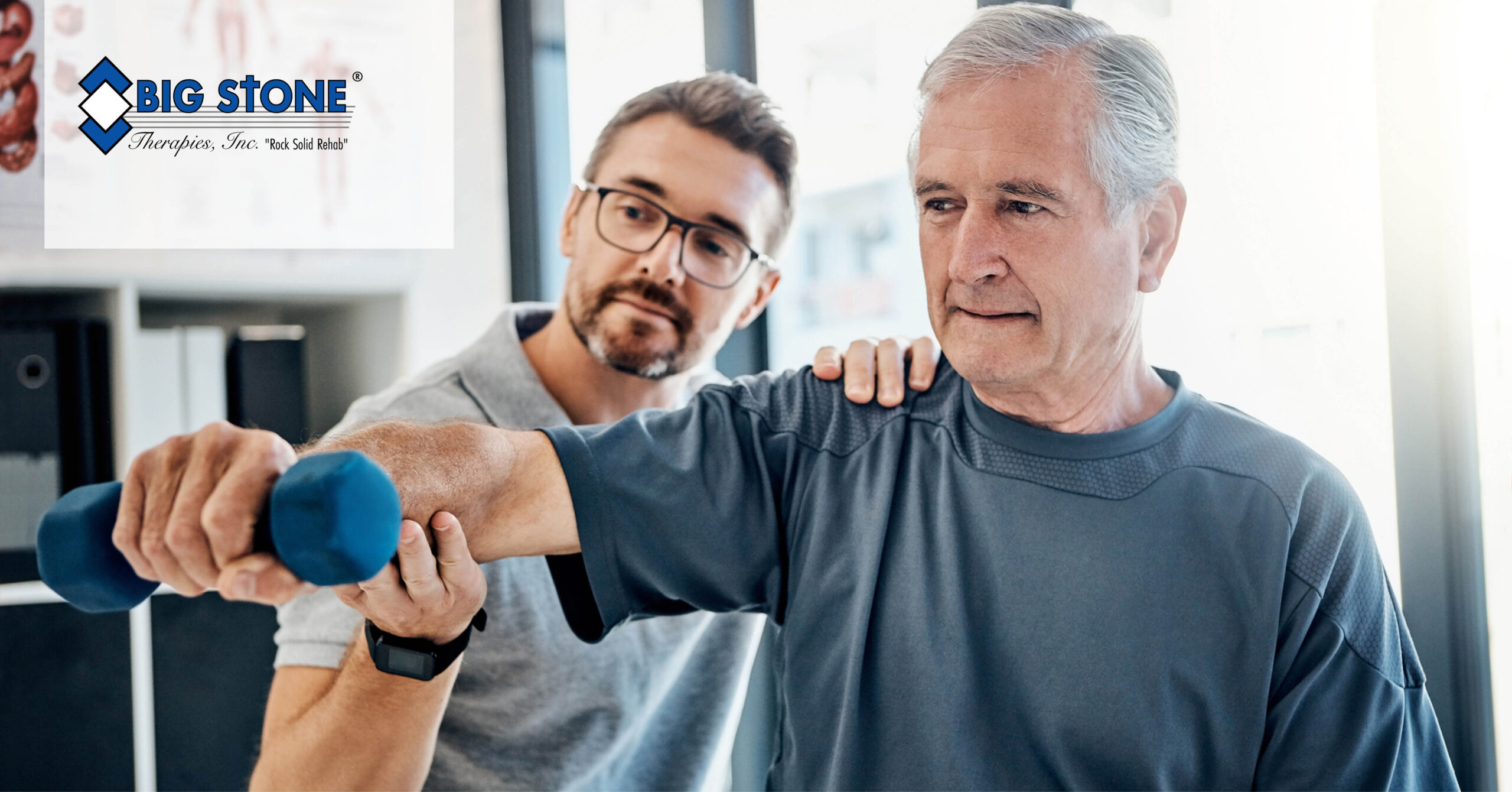 An elderly man in a blue shirt lifts a blue dumbbell, assisted by a younger man wearing glasses in a light room. The atmosphere is supportive and focused.
