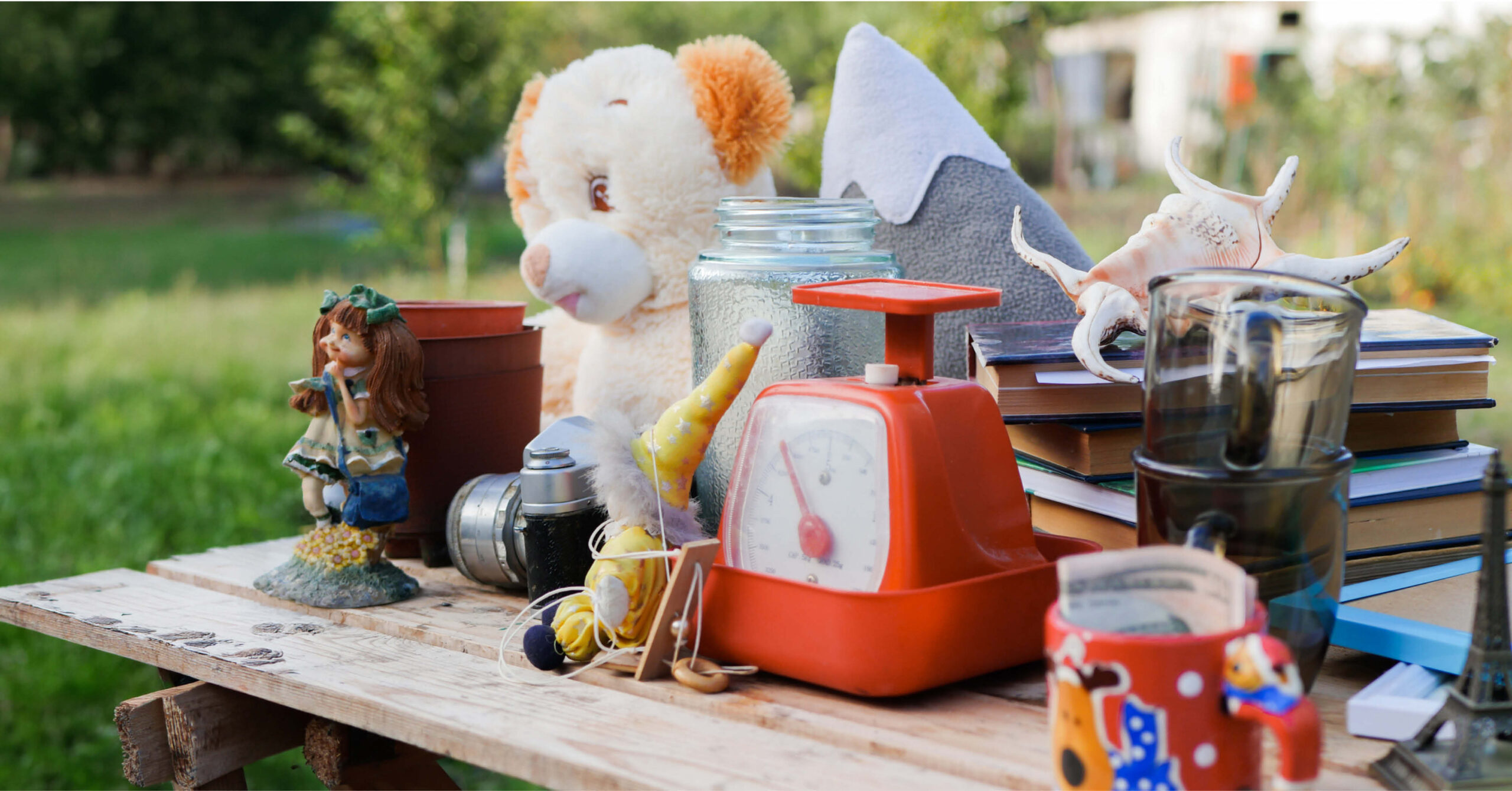 A variety of items including toys, a clock, and books on a table in a garden.